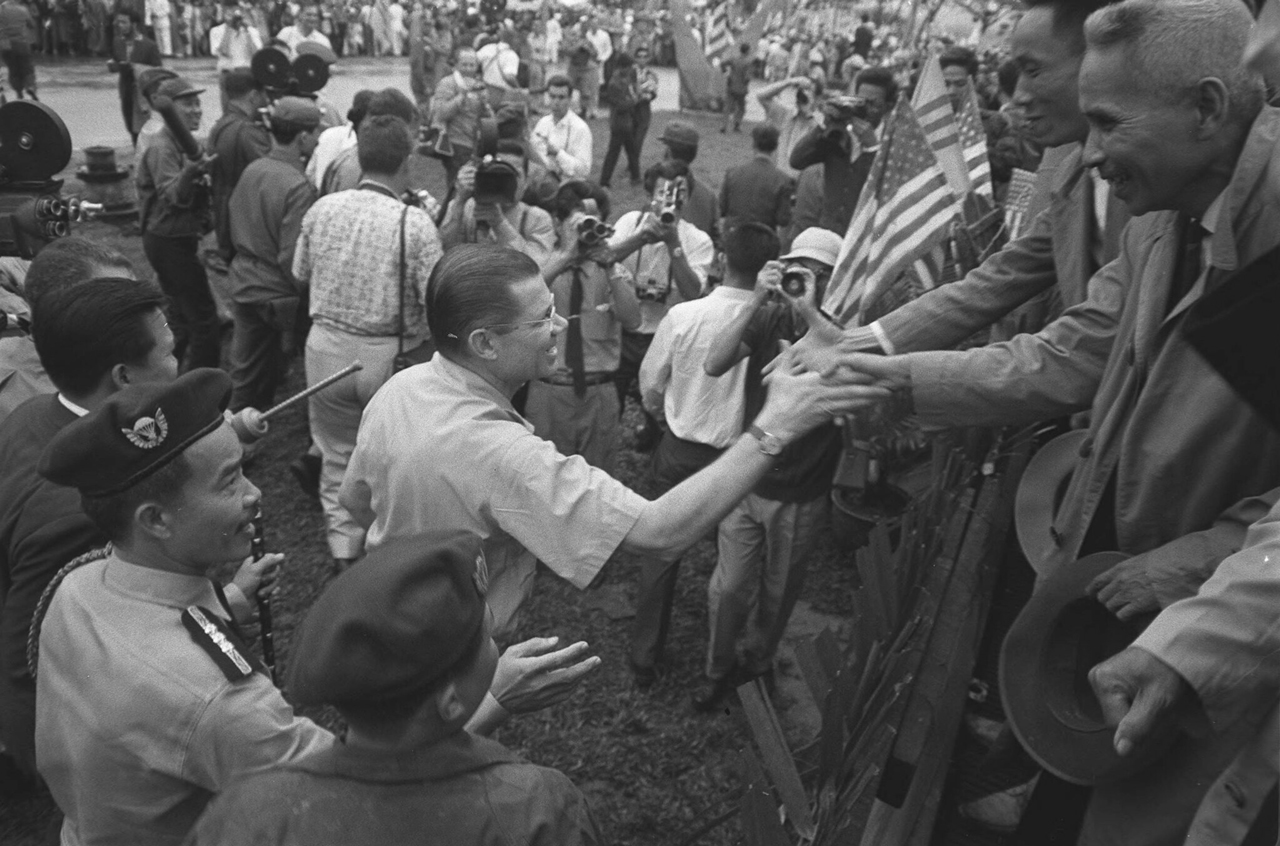 McNamara đến thăm làng Hòa Hảo cùng với Khánh bắt tay những người dân Việt Nam tháng 3 năm 1964